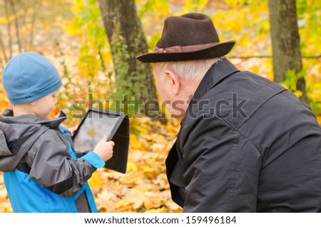 Young boy using a tablet pc with his disabled grandfather in a wheelchair watching