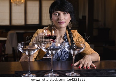 Attractive stylish woman smiling as she sits alone drinking a glass of red wine at the bar in a nightclub