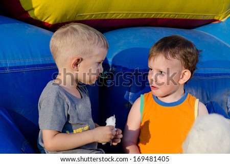 Two cute little boys enjoying cotton candy or candy floss together in the summer sunshine smiling in enjoyment of the treat