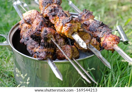 Barbecued food on metal skewers resting on a pot outdoors.