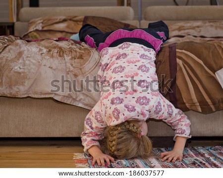 Little girl hanging off the side of a bed balancing her head and hands on the floor as she amuses herself playing