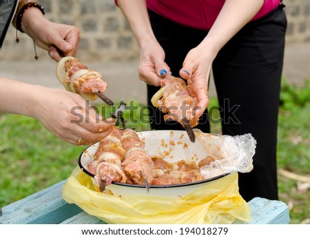 Closeup of the hands of a young woman preparing kebabs to grill on a BBQ threading spicy meat and onions from a basin onto metal skewers