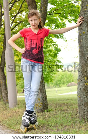 Sporty teenage girl on roller blades standing leaning against a tree alongside a rural road watching something with a thoughtful expression
