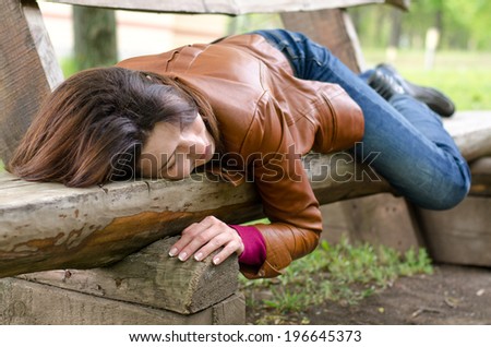 Exhausted stylish woman in a leather jacket lying on her back sleeping on a wooden bench in rural countryside