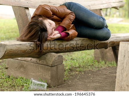 Drunk woman sleeping it off on a wooden bench in a park lying face down in her leather jacket fast asleep