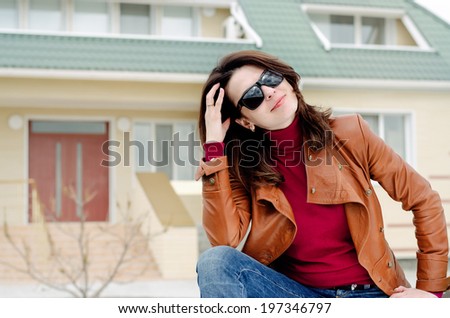 Woman in Sunglasses Sitting in front of her house with her hand behind her head.
