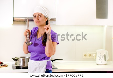 Woman chef having a brainwave as she tastes the food in the saucepan from a ladle raising her finger as she thinks of a new or missing ingredient