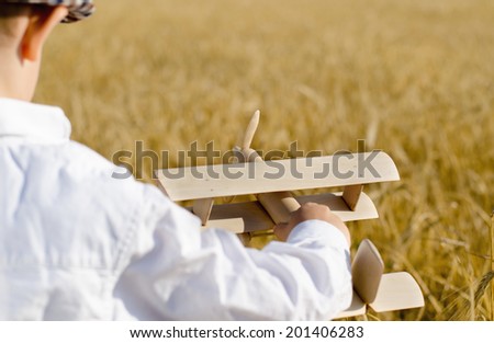 Cute little boy flying his toy plane in a wheat field standing in the ripening golden ears of wheat swooping and climbing in the air as he imagines himself to be the pilot
