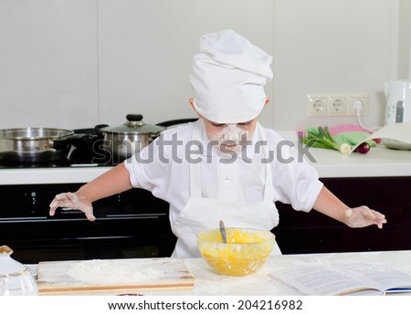 Cute little boy in a chefs uniform baking a cake in the kitchen adding ingredients from the recipe into his mixing bowl