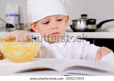 Little boy following a recipe as he bakes a cake reading the list of ingredients to be added to the eggs in his mixing bowl