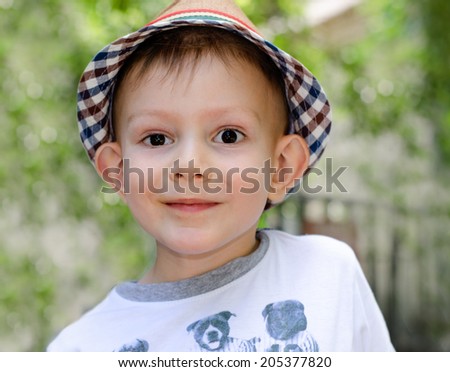 Cute little boy with a wide-eyed expression wearing a stylish checked hat looking directly into the camera with a friendly smile
