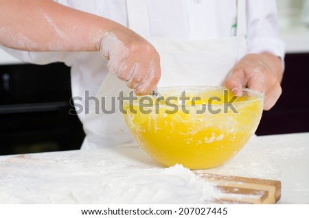 Little boy mixing cake ingredients in a mixing bowl whipping the flour and eggs to make the dough