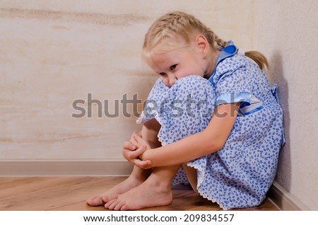 Sad young girl sitting in the corner feeling sorry