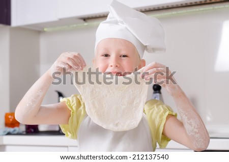 Cute proud little girl in a chef or cooks toque and apron holding up her rolled out pastry for a homemade pizza with a beaming smile