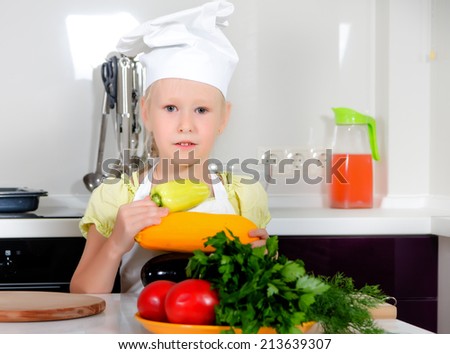 Cute little girl learning to be a chef standing with an assortment of farm fresh vegetables in the kitchen dressed in a white toque and apron