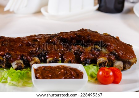 Close Up of Rack of Saucy Barbecue Pork Ribs with Dipping Sauce Served on Plate in Restaurant