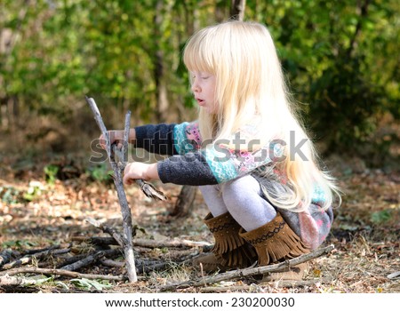 Close up Cute Little Blond Girl Playing with Dry Twigs on Ground at the Woods During Autumn Season. Captured in Side View.