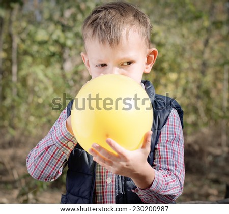Small boy blowing up a colorful yellow party balloon with a look of concentration as he stands outdoors in the garden