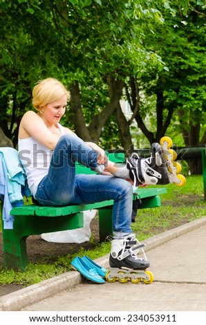Attractive blond woman sitting on a park bench putting on roller blades as she prepares for a fun day skating