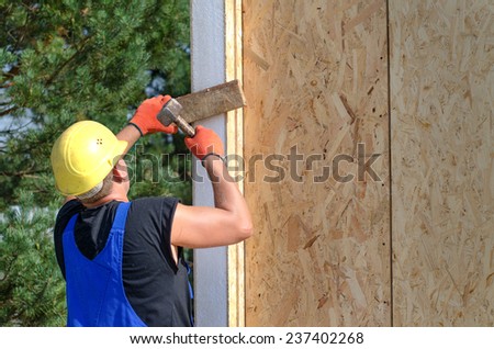 Builder hammering on a wooden wall panel using a mallet as he installs an upright beam on a new build house