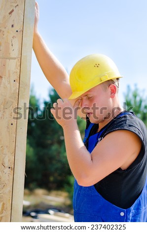 Close up of a young builder in a hardhat and dungarees working on a building site supporting a wooden beam in the upright position with his hand