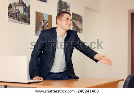 Businessman with a warm friendly smile standing up to shake hands over his desk in welcome, congratulations or to finalize a business deal or partnership