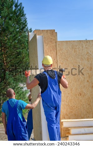 Two builders installing an insulated wooden wall panel on a construction site for a new build house working outdoors in the sunshine