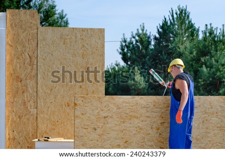 Builder applying glue to an insulated wooden wall panel on a building site for a new build house