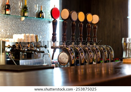 Beer taps behind a deserted bar counter for dispensing draft beer from a large storage keg below the wooden counter
