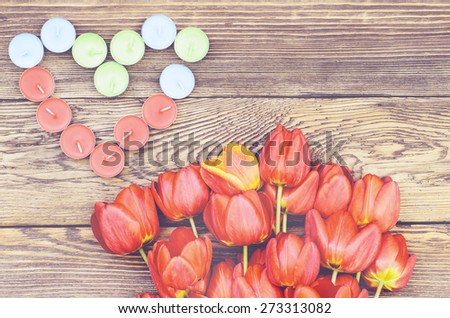Bunch of fresh red tulips lying alongside a a heart formed of colorful candles for a loved one or sweetheart on Valentines Day or an anniversary, overhead view