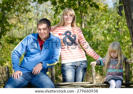 Parents and Daughter Taking a Pose at the Garden Fence with Tree Leaves Shades in Autumn Outfits.