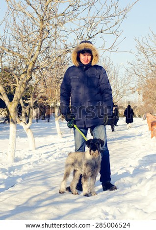 Full Length Shot of an Adult Man in Winter Outfit with his Dog Standing at the Snow and Looking at the Camera.