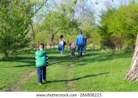 Rear View of Family Walking Together Outdoors on Overgrown Dual Track Country Road Through Green Trees