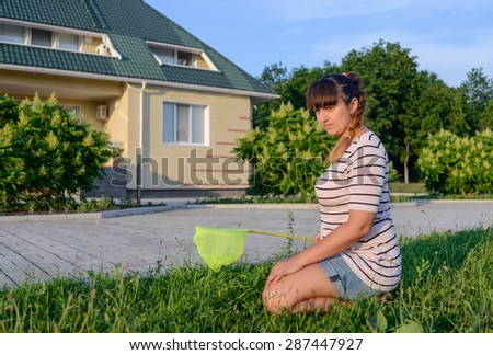 Serious Woman with Bug Net Crouching on Grass on Lawn in front of Contemporary Home