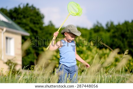 Young Boy with Bug Net Exploring Long Grass in front of Home Outdoors in Summer