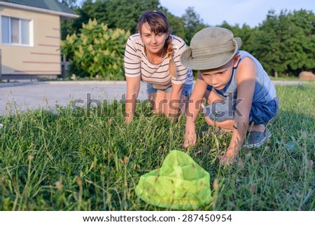 Little boy catching insects in a net with his mother as they both crouch down in the fresh green spring grass as he makes his catch