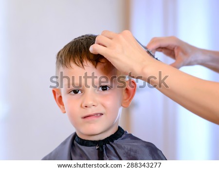 Hairdresser cutting a little boys hair into a short hairstyle in her salon