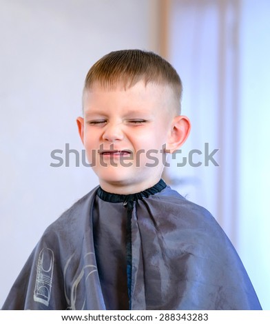Young Boy Grimacing with Eyes Closed While Getting Hair Cut - Boy Wearing Apron Making a Face and Not Enjoying Getting His Hair Cut