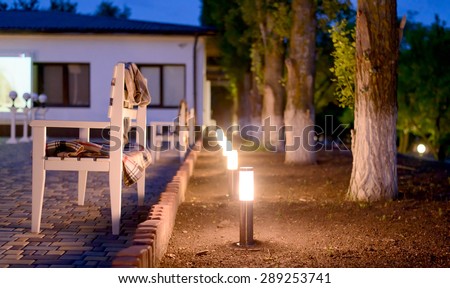 Row of Illuminated Outdoor Lights in Ground Alongside Stone Patio Furnished with Wooden Benches and Plaid Blankets Creating a Cozy and Inviting Atmosphere