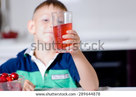 Happy Boy Looking Surprised at Taste of Red Juice in Glass While Sitting at Kitchen Table with Bowl of Ripe Cherries