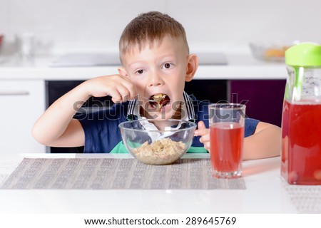 Young Boy Eating Oatmeal Cereal for Breakfast at Kitchen Table, with Glass of Red Juice