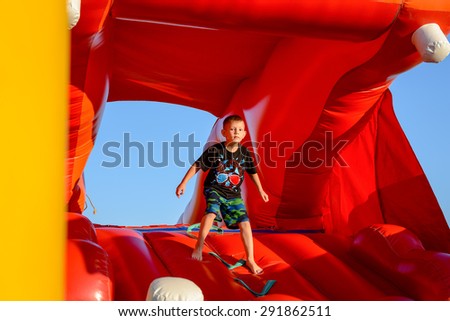 Waist up of blond boy (7-9 years) wearing black t-shirt with colorful print playing in red bouncy castle