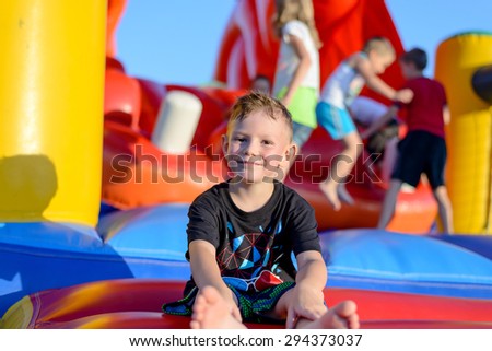 Smiling happy barefoot little boy sitting on a colorful inflatable plastic jumping castle at a fairground or kids playground