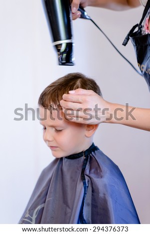 Little boy having his hair blow dried with a hairdryer in a hairdressing salon after a hair cut