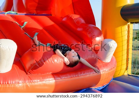 Smiling boy (7-9 years) wearing black t-shirt lies upside down on slide of red bouncy castle