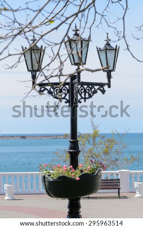 Ornate wrought iron lamppost with flowers on a coastal esplanade overlooking a calm ocean