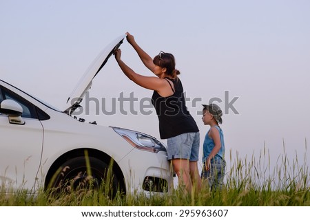 Mom with Son Looking at the Camera While Opening the Front of a Defective Car at the Grassy Ground.