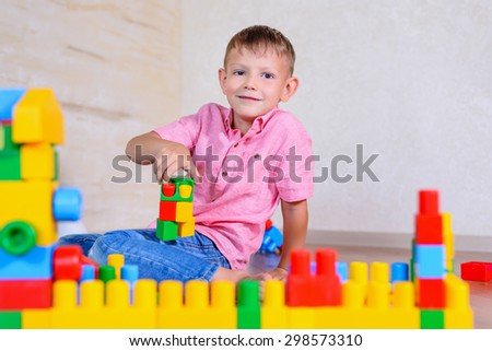 Happy young boy playing with his building blocks holding a finished creation in his hands as he grins cheekily at the camera