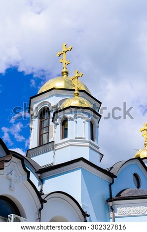 Traditional Christian Orthodox white church with golden domed tower bell and crosses under a cloudy sky