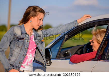 Two women chatting at the roadside with a young woman leaning against a car chatting to the female driver, close up view